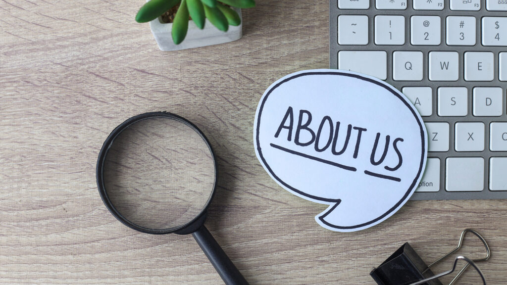An about us speech bubble cut out and places on a keyboard and desk.