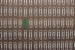 One green paperclip among dozens of white paperclips.