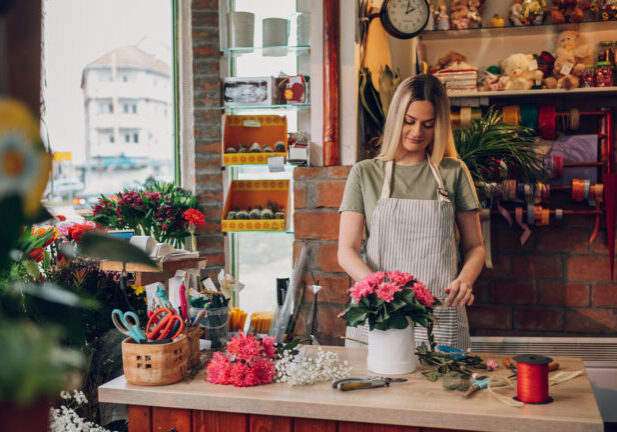Graceful female florist making a beautiful bouquet in a round box while wearing an apron and working in a flower shop. Florist workplace. Small business concept.